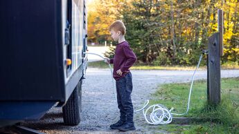 Little Boy Connecting Water Hose to Camper Trailer on Campground in Autumn, Quebec, Canada