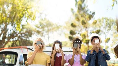 Vier junge Erwachsene stehen mit dem Smartphone vor dem Gesicht da