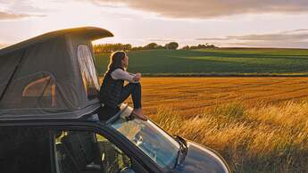 Woman sitting on roof of campervan at sunset